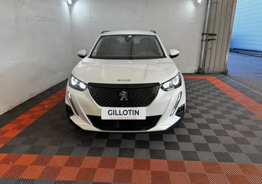 Peugeot 2008 blanc vue de face en intérieur, avec calandre noire et phares LED allumés.