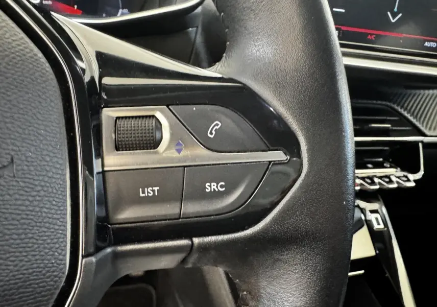 Gros plan sur le volant cuir noir multifonctions de la Peugeot 2008 blanc, avec commandes audio et téléphone intégrées.