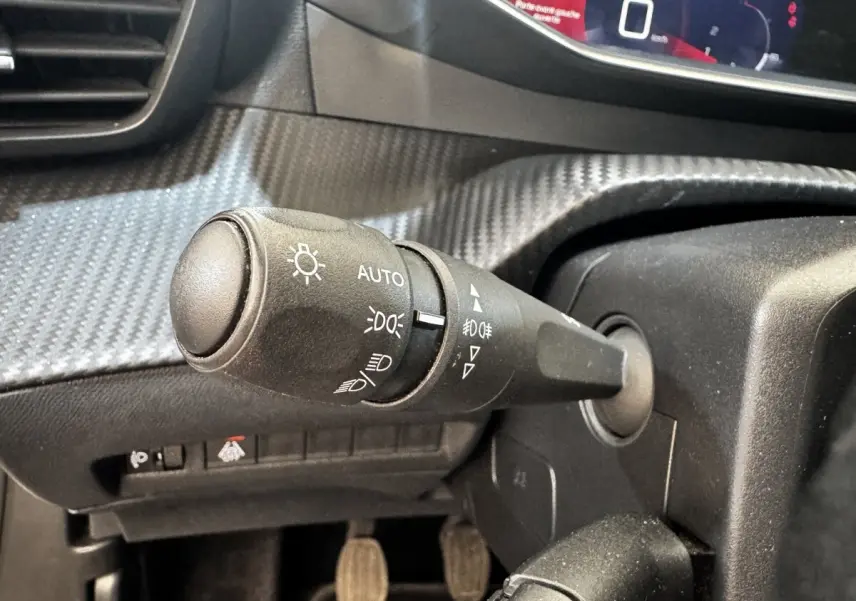 Gros plan sur la commande des feux avec réglage automatique dans l’habitacle noir du Peugeot 2008 blanc, version Allure Business.