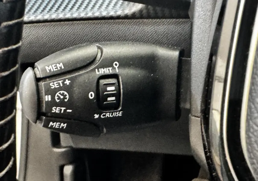 Gros plan sur la commande de régulateur de vitesse noire à gauche du volant dans l’habitacle d’un Peugeot 2008 blanc.