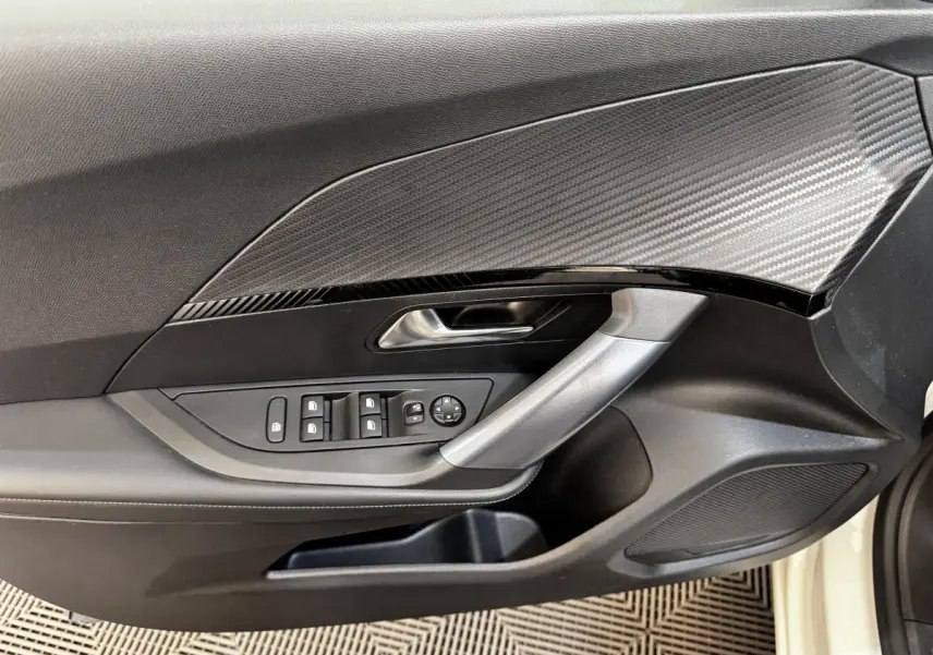 Vue rapprochée de la porte avant gauche blanche du Peugeot 2008 avec commandes électriques et insert décoratif carbone.