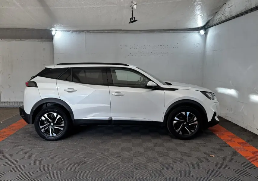 Peugeot 2008 blanc vue de profil côté gauche dans un garage, avec jantes noires et toit noir contrastant.