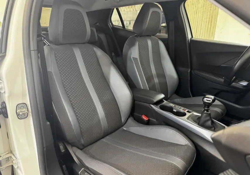 Vue intérieure côté avant gauche du Peugeot 2008 blanc, mettant en valeur les sièges tissu et cuir et la boîte manuelle.