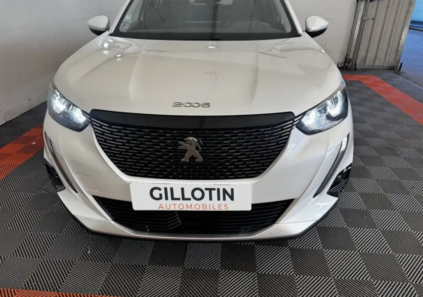 Vue de face d’un Peugeot 2008 blanc avec calandre noire et phares LED allumés dans un garage.