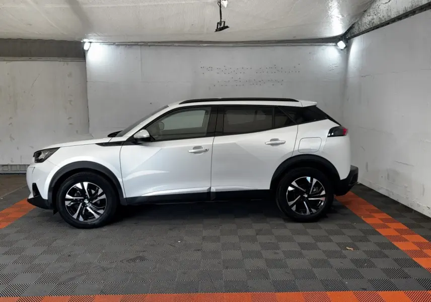 Peugeot 2008 blanc vue de profil côté gauche, avec toit noir et jantes alliage bicolores dans un garage.
