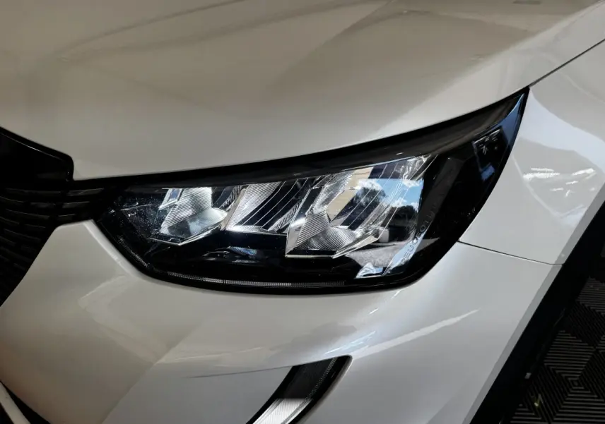 Gros plan sur le phare avant droit blanc du Peugeot 2008, mettant en valeur le design moderne et les détails lumineux.