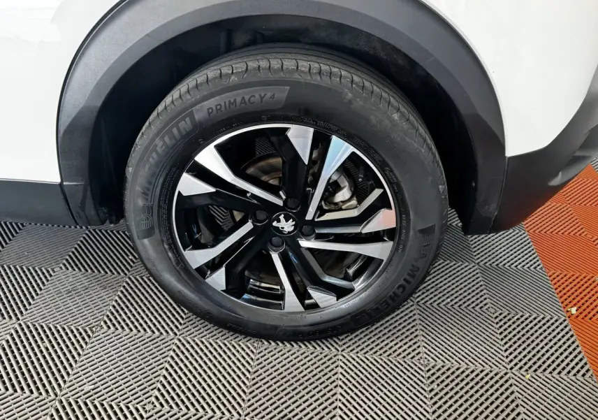 Gros plan sur la roue arrière droite d’un Peugeot 2008 blanc avec jante alliage noire et argentée.