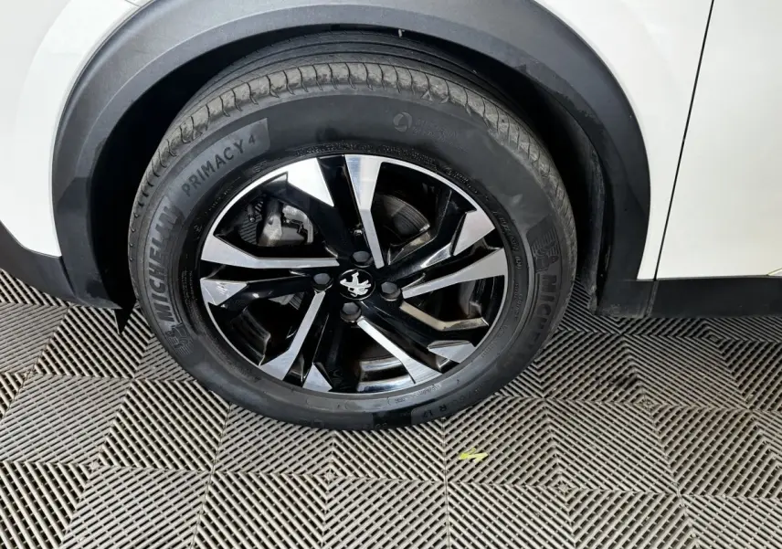 Gros plan sur la roue avant gauche noire et argentée du Peugeot 2008 blanc, avec jante au design moderne.