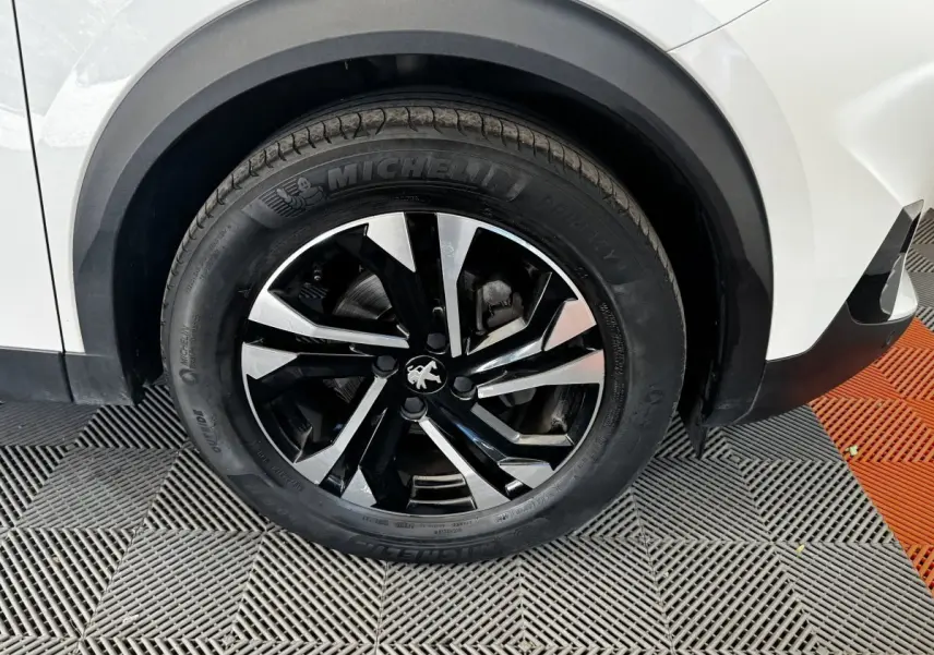 Gros plan sur la roue avant droite noire et argentée d'un Peugeot 2008 blanc avec partie de l'aile visible.
