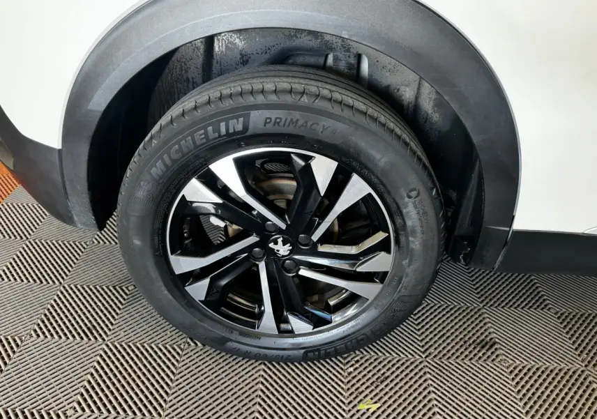 Gros plan sur la roue arrière droite d’un Peugeot 2008 blanc avec jante alliage noire et argentée.