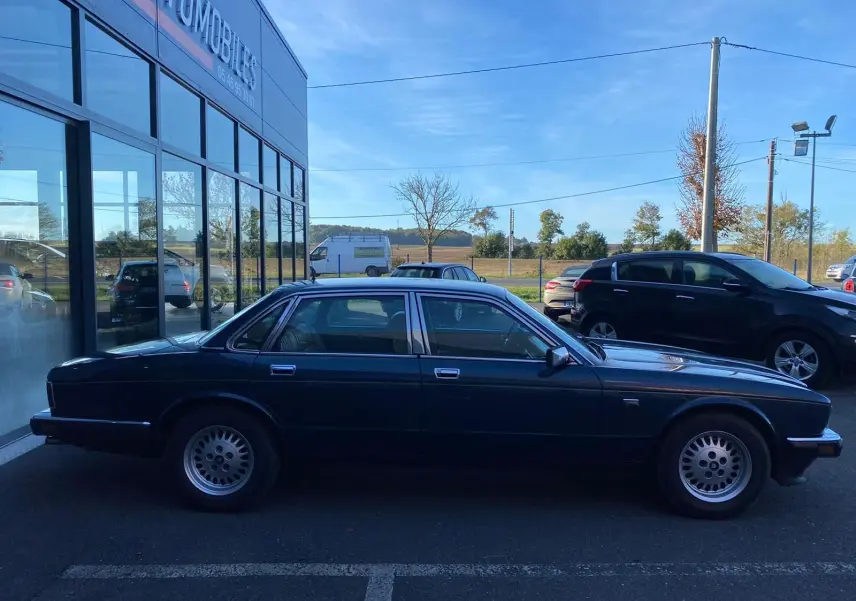 Profil côté droit d'une Jaguar XJ6 3.6 Sovereign bleu foncé de 1987, élégante berline classique aux jantes d'origine.
