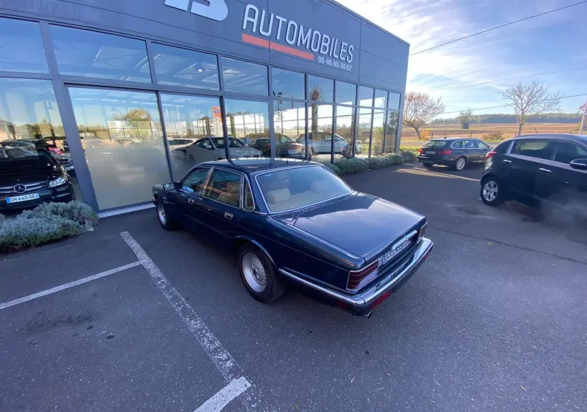 Jaguar XJ6 3.6 Sovereign bleu vue 3/4 arrière côté gauche, garée devant un showroom avec plusieurs autres voitures.
