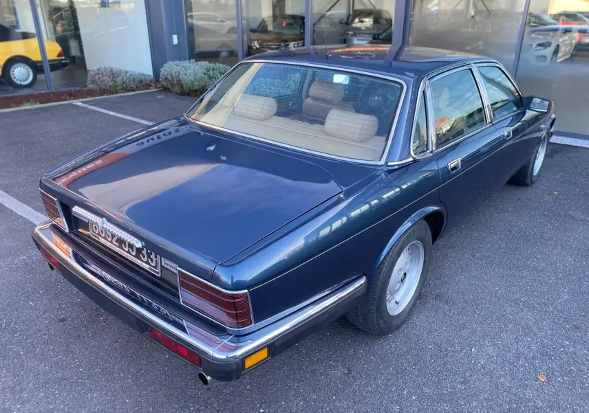 Vue 3/4 arrière droite d'une Jaguar XJ6 3.6 Sovereign bleu 1987 avec intérieur beige et jantes classiques.