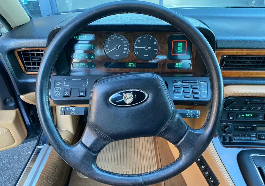 Vue intérieure centrée sur le volant noir et le tableau de bord en bois d'une Jaguar XJ6 3.6 Sovereign bleu de 1987.