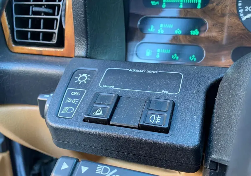 Gros plan sur le tableau de bord de la Jaguar XJ6 3.6 Sovereign 1987, avec commandes d'éclairage et bois verni.