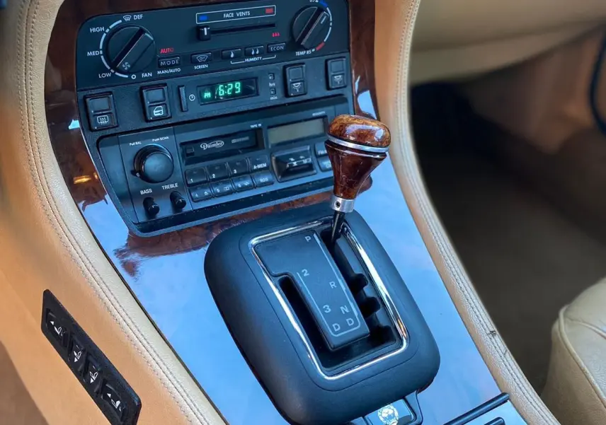 Gros plan sur la console centrale beige avec levier de vitesses bois et commandes d’origine d’une Jaguar XJ6 3.6 Sovereign 1987.