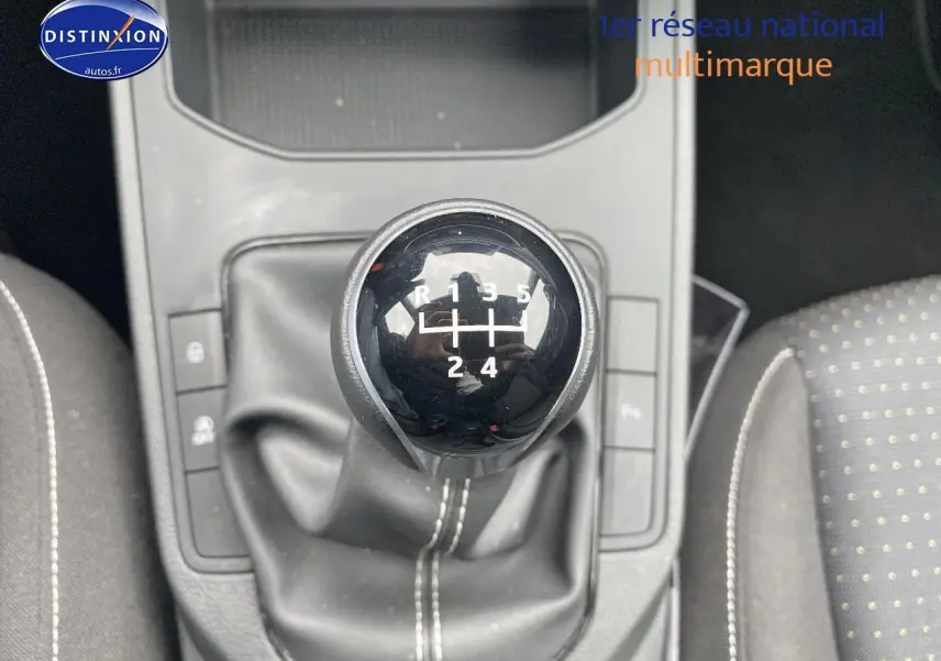 Gros plan sur le levier de vitesse manuel noir de la SEAT Ibiza 1.0 TSI 95 Copa, avec coutures blanches et sièges tissu gris à pois.