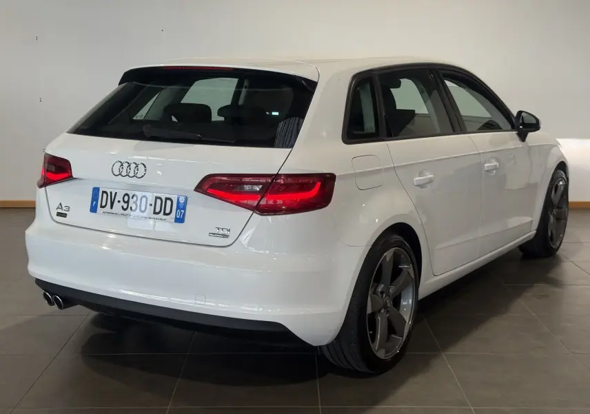 Audi A3 Sportback blanc vue 3/4 arrière droit, feux allumés et jantes alliage foncé distinctives.