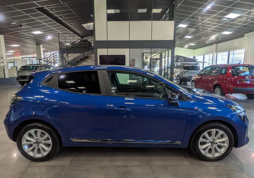 Profil côté gauche d'une Renault Clio V Bleu Iron 2025 en intérieur, soulignant ses jantes alliage et lignes fluides.
