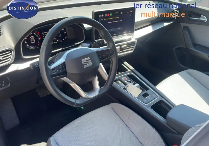 Vue intérieure côté conducteur du tableau de bord et volant cuir noir de la SEAT LEON 2025 blanc, avec écran tactile central.