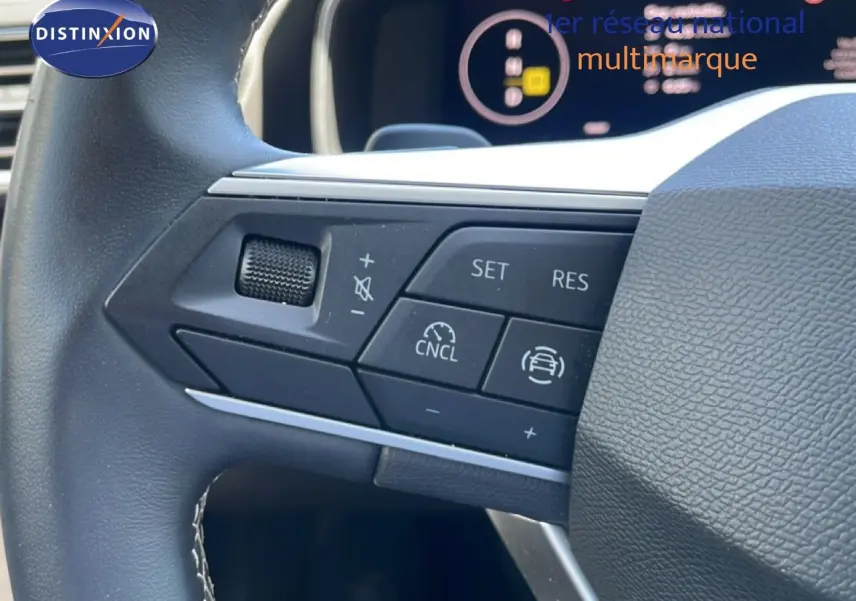 Gros plan sur les commandes au volant à gauche du SEAT LEON blanc 2025, avec régulateur de vitesse et boutons multifonctions.