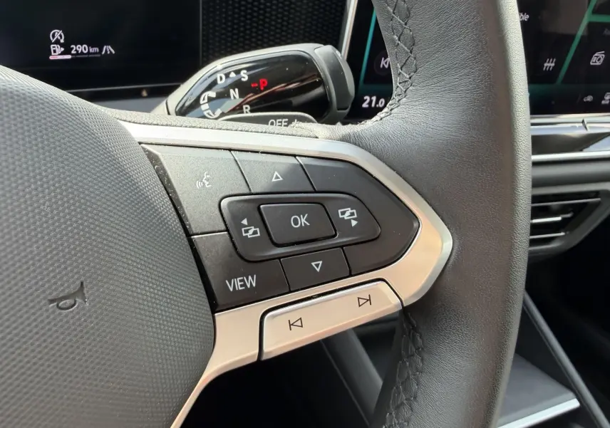 Gros plan sur les commandes multifonctions du volant cuir noir du Volkswagen Tiguan 2025, avec levier de vitesses en arrière-plan.