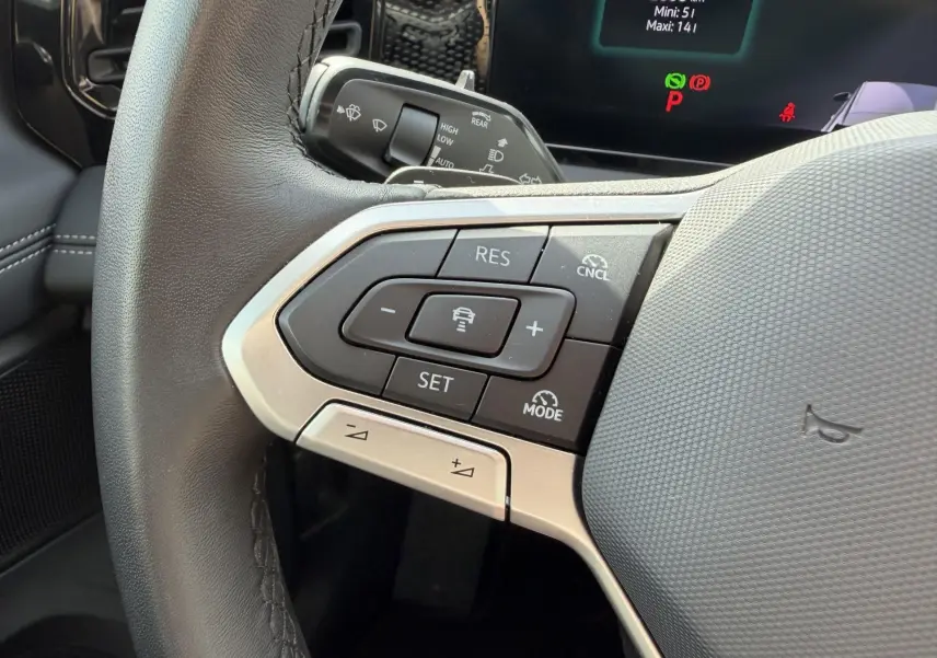 Gros plan sur les commandes du volant cuir noir du Volkswagen Tiguan 2025, avec affichage digital en arrière-plan.