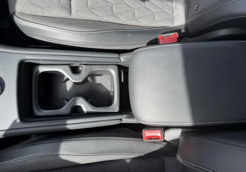 Vue plongeante sur la console centrale noire du Volkswagen Tiguan 2025, avec porte-gobelets et accoudoir en cuir.