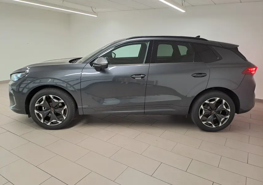 Vue de profil côté gauche d'un CUPRA TERRAMAR gris Timanfaya avec jantes 19'' Cosmic usinées en intérieur showroom.