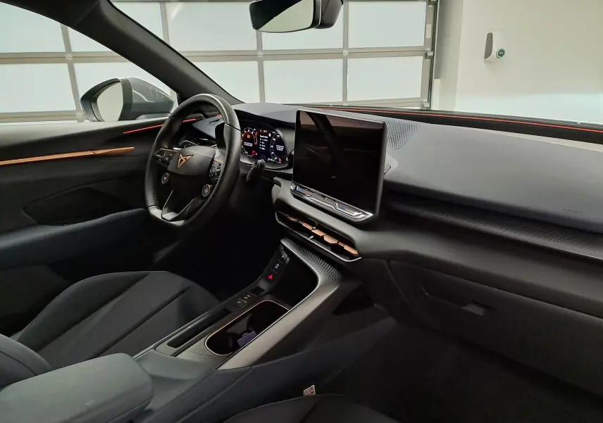 Vue intérieure côté conducteur du CUPRA TERRAMAR 2025, tableau de bord noir avec éclairage ambiant cuivré et écran tactile central.