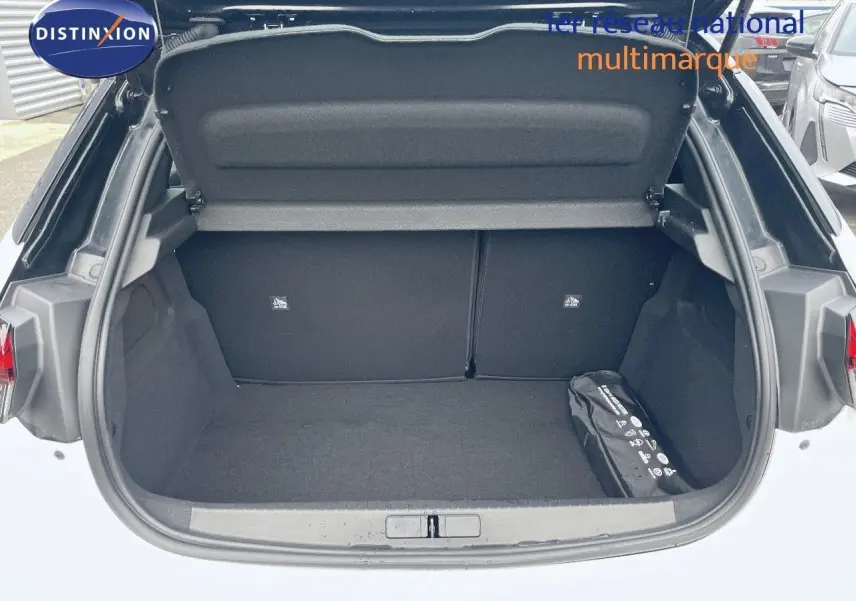 Coffre ouvert vu de l'arrière d'une Opel Corsa blanche 2022, avec un kit de sécurité noir dans le coffre.