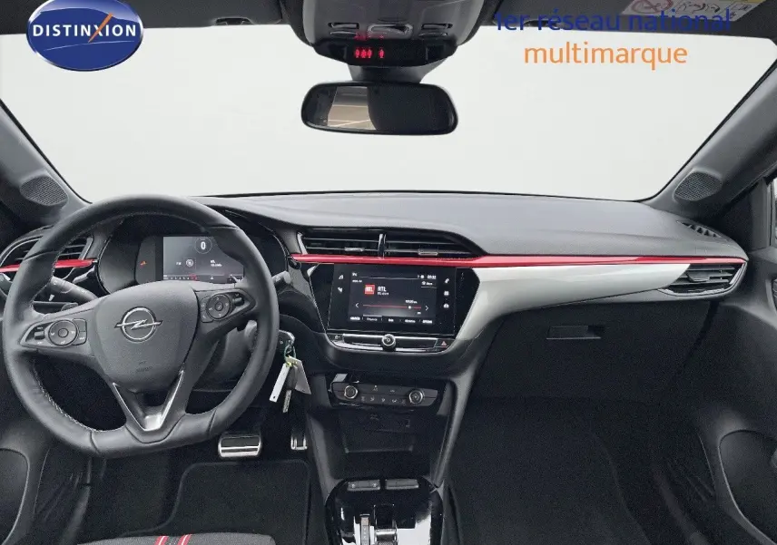 Intérieur de l'Opel Corsa blanc 2022 vu de face, tableau de bord noir avec bande rouge et écran tactile central.