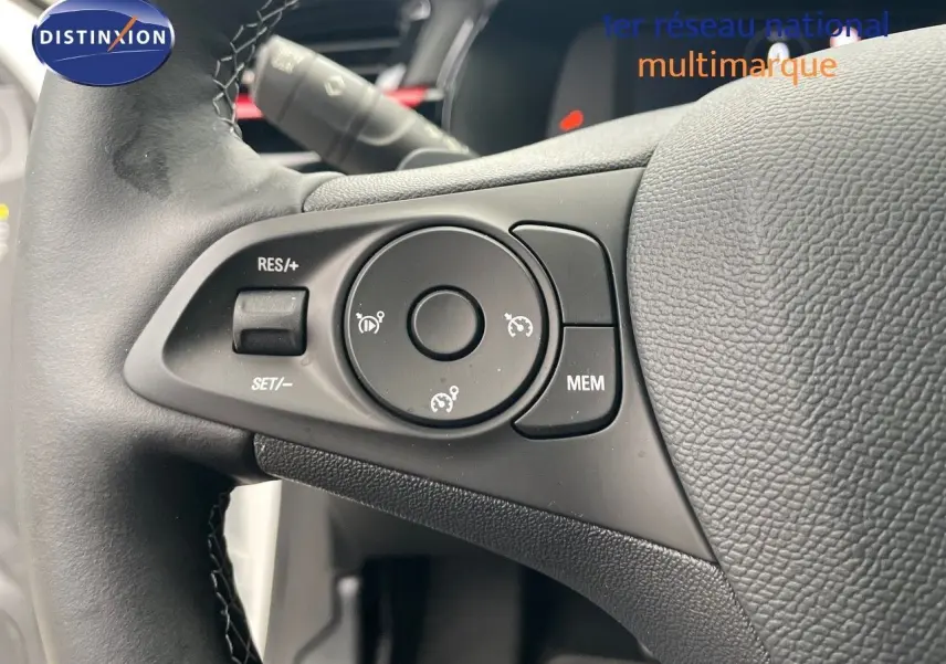 Gros plan sur les commandes du régulateur de vitesse au volant cuir noir d'une Opel Corsa blanche de 2022.
