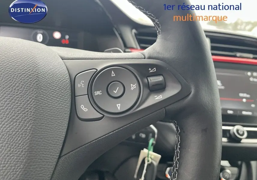 Gros plan sur le volant en cuir noir de l'Opel Corsa blanc, avec commandes audio intégrées et tableau de bord en arrière-plan.