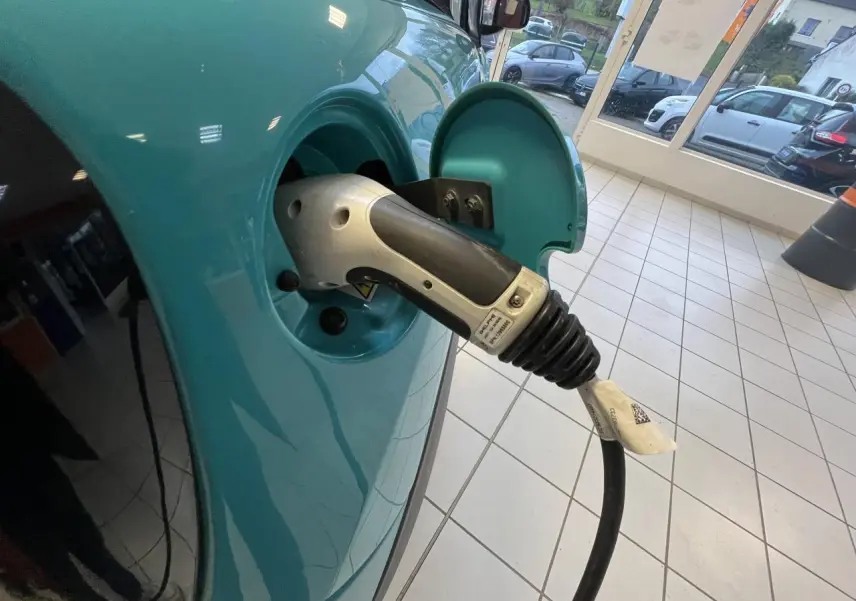 Prise de recharge branchée sur le côté gauche d'une Citroën E-MEHARI cabriolet bleu clair en intérieur showroom.