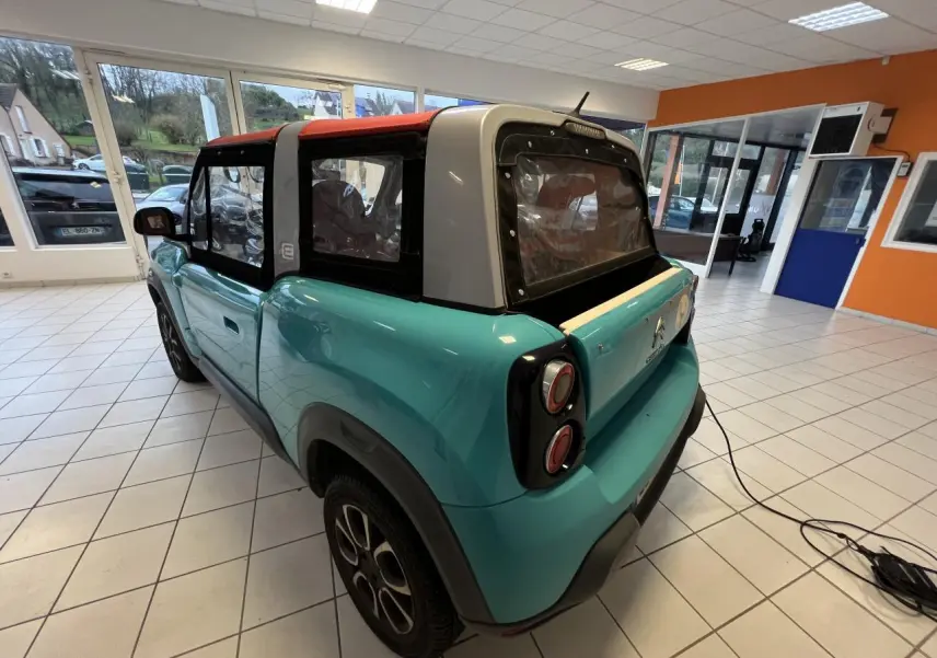 Vue 3/4 arrière droite du cabriolet Citroën E-MEHARI bleu clair avec toit en toile rouge et jantes alliage 15 pouces.
