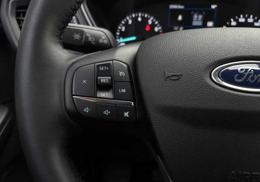 Gros plan sur le volant cuir noir du Ford Kuga 2024, avec commandes multifonctions et logo Ford visible au centre.