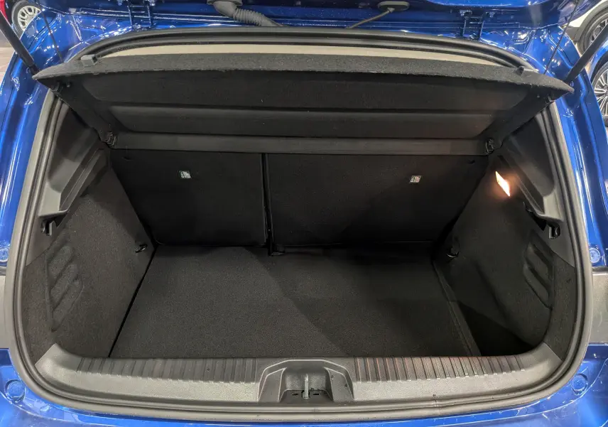 Coffre ouvert vu de l'arrière d'une Renault Clio V Bleu Iron, montrant l'espace de chargement et l'éclairage intérieur.