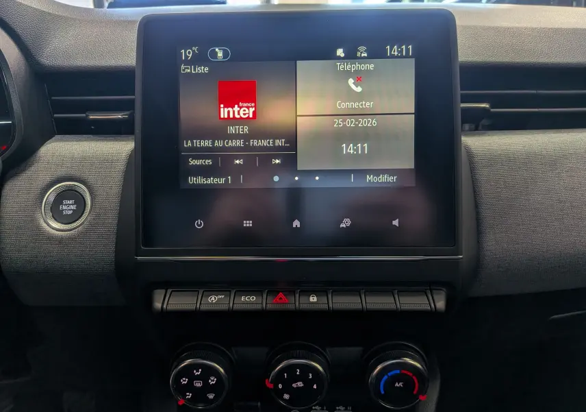 Vue rapprochée de l’écran tactile central et des commandes de climatisation du tableau de bord d’une Renault Clio V Bleu Iron.