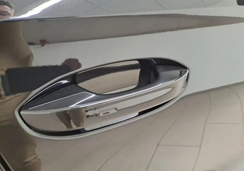 Poignée de porte chromée en gros plan sur une CUPRA Leon Noir Minuit, reflétant l'intérieur lumineux.