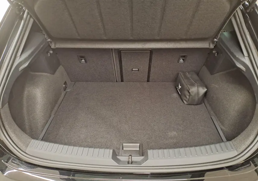 Coffre ouvert vu de l'arrière d'une CUPRA Leon Noir Minuit avec tapis gris et trousse de secours sur le côté droit.
