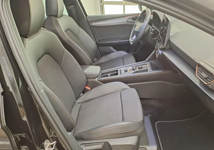 Vue intérieure côté conducteur de la CUPRA Leon 2025 noir minuit, sièges en cuir avec surpiqûres contrastées et tableau de bord moderne.