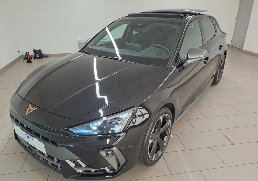 Vue 3/4 avant droite d'une CUPRA Leon 2025 Noir Minuit avec toit ouvrant panoramique et projecteurs Matrix LED allumés.