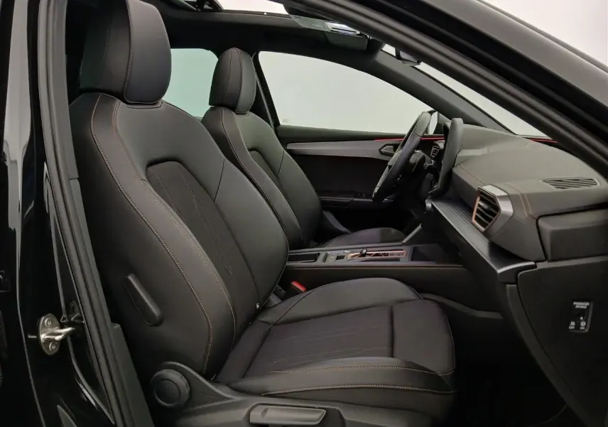 Vue intérieure côté gauche de la CUPRA Leon 2025 avec sièges noirs, surpiqûres orange et toit ouvrant panoramique visible.