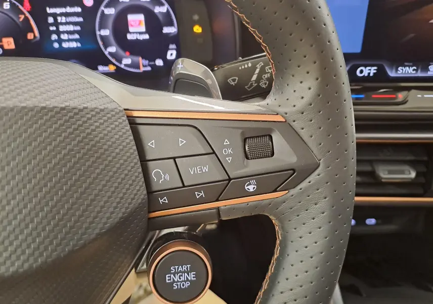 Gros plan sur le volant côté droit de la CUPRA Leon 2025, avec boutons multifonctions et démarreur intégré, ambiance intérieure noire et cuivre.