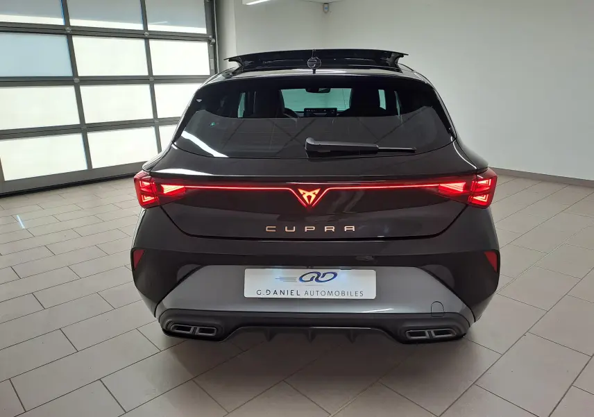 Vue arrière d'une CUPRA Leon 2025 Noir Minuit avec feux LED allumés et double sortie d'échappement intégrée.