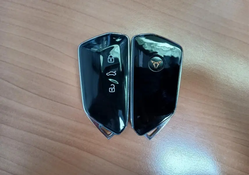 Clé de voiture CUPRA noire brillante avec logo doré, vue rapprochée sur fond bois clair.