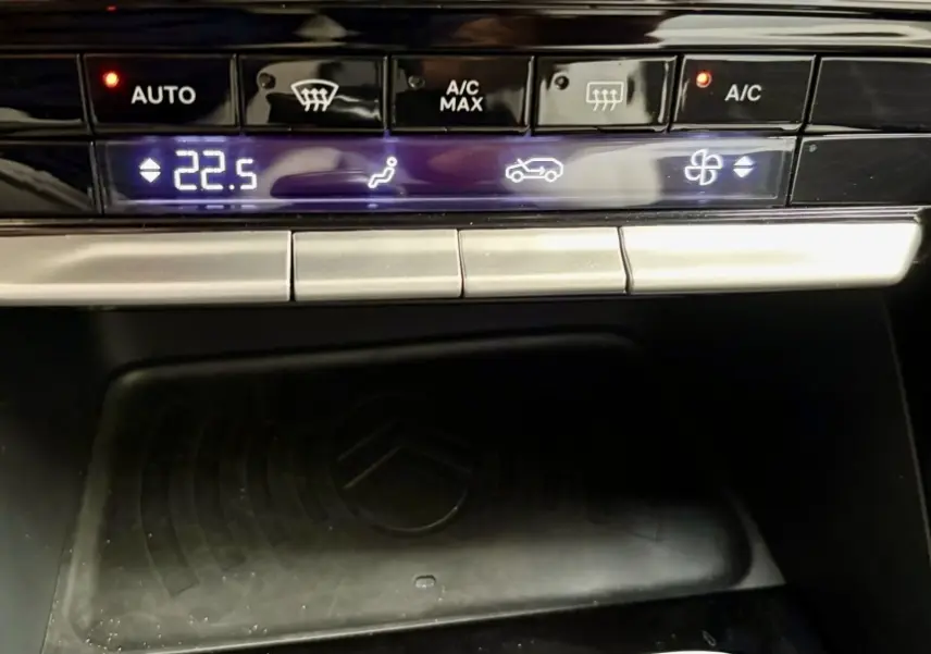 Gros plan sur la commande de climatisation digitale et zone de recharge par induction noire dans une Citroën C3 rouge 2025.