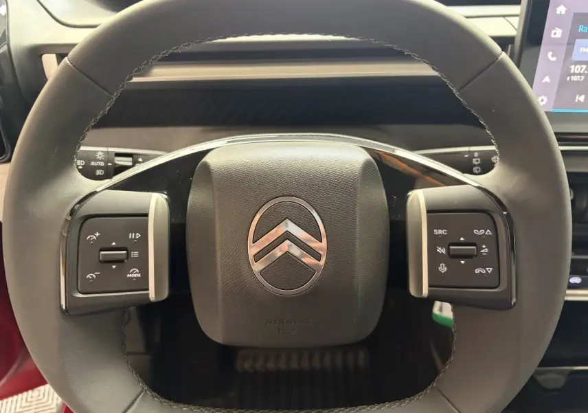 Gros plan sur le volant cuir multifonctions de la Citroën C3 Turbo 100 BVM6 MAX rouge, avec commandes intégrées.
