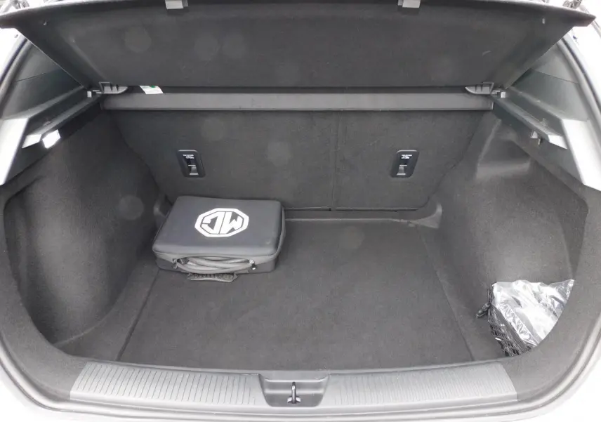 Coffre ouvert d'une MG4 blanche 2023, montrant un sac de recharge noir avec logo MG posé à l'intérieur.